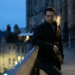 Detective Sergeant John Rebus (played by Richard Rankin) wearing a black jacket in Edinburgh old town