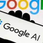 A Google AI logo is on a phone held in a hand, in front of a Google Logo