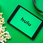 A tablet with the Hulu logo surrounded by popcorn, soda, headphones and a cactus