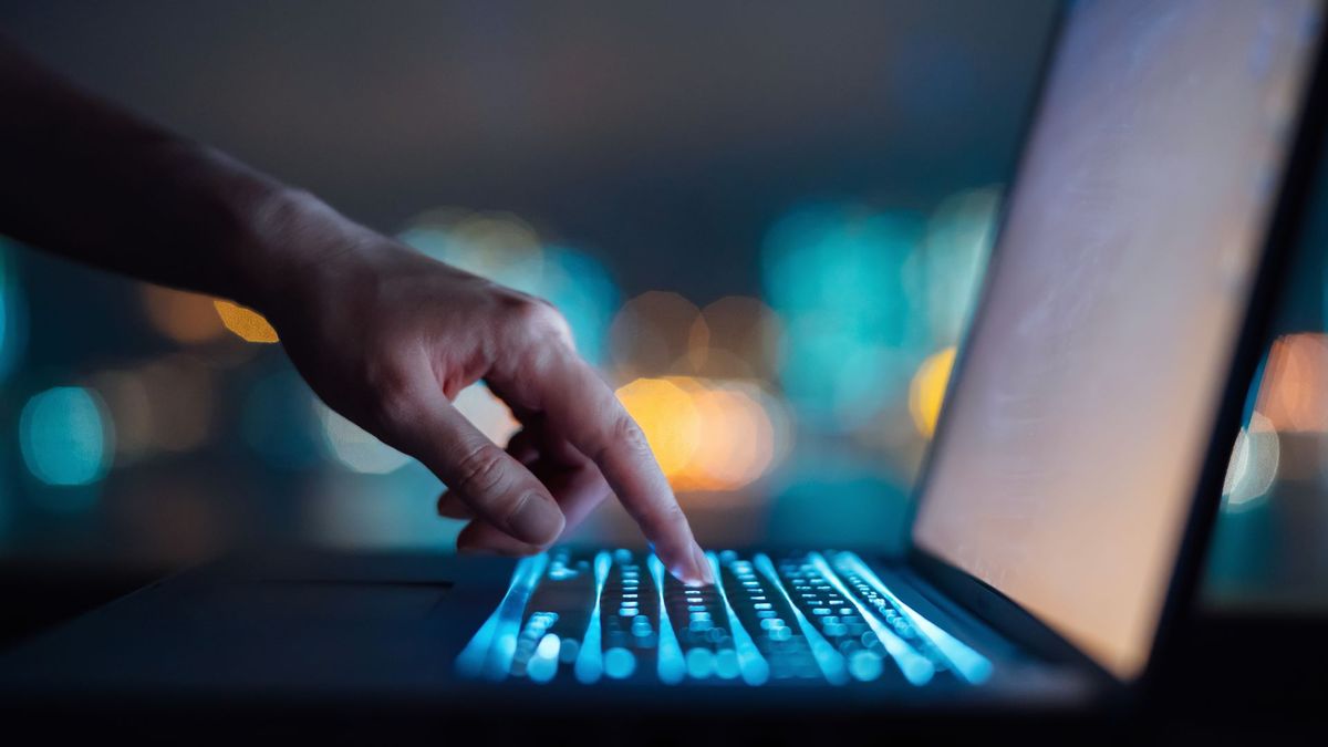 A person typing on a computer, lit up by the screen