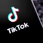 The TikTok logo displayed on a smartphone screen with a computer keyboard in the background.