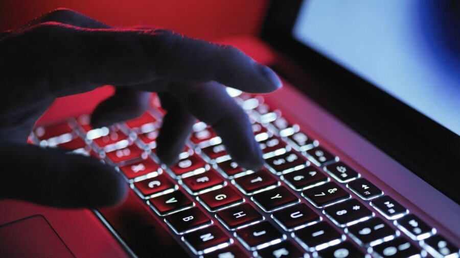 A hand typing at a computer in a dark room, lit up by the laptop