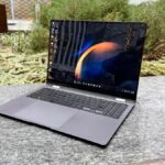 A laptop sitting on a backyard table with plants in the background.