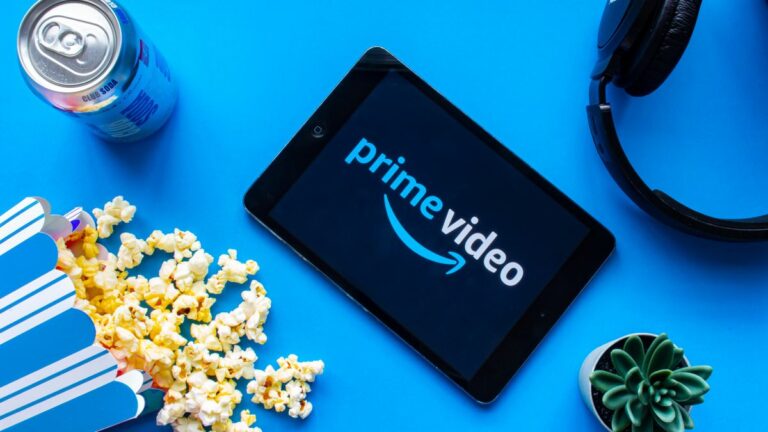 Prime Video logo appears on a tablet surrounded by a can of soda, spilled popcorn, headphones and a cactus