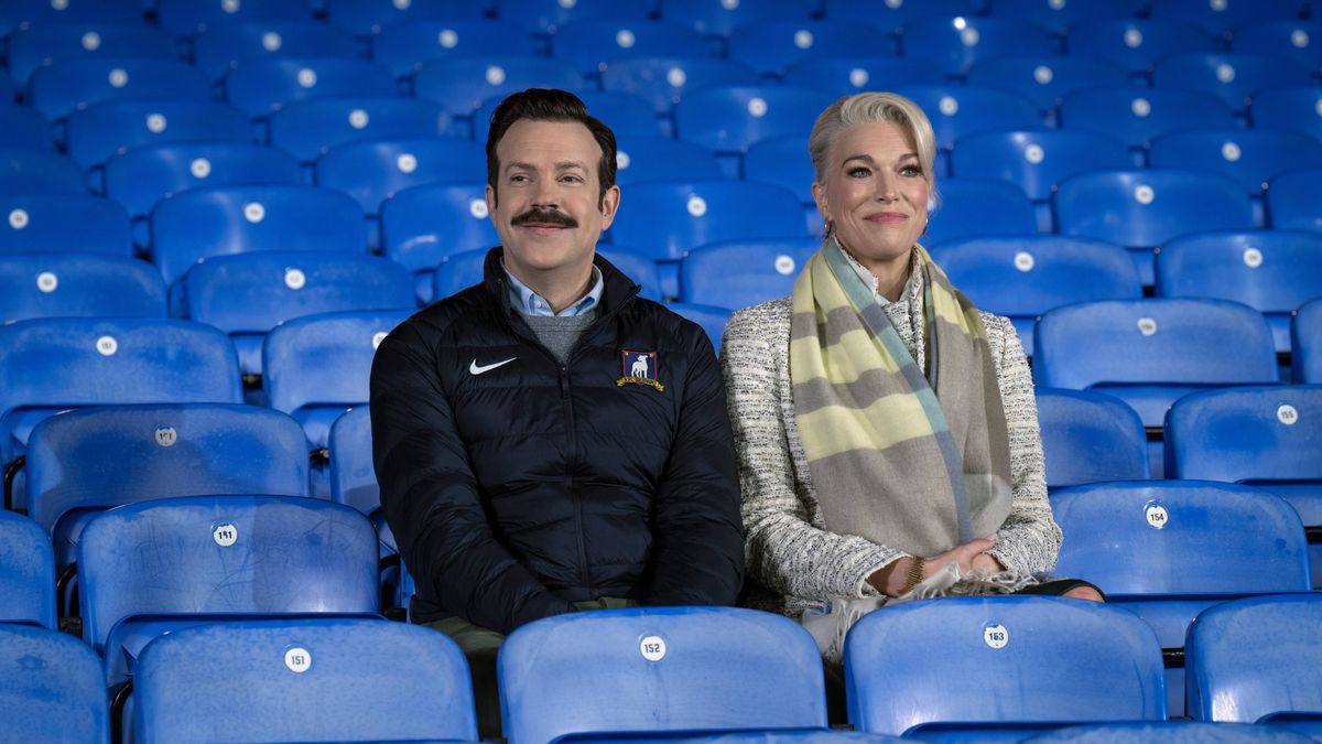 Ted Lasso (Jason Sudeikis) and Rebecca Welton (Hannah Waddingham) sitting in the stands in