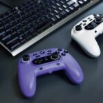 A violet and white Wireless Horipad for Steam controllers sitting on a desk in front of a keyboard.