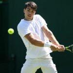 Carlos Alcaraz plays a backhand all in white on court at Wimbledon 2024.