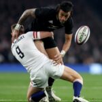 An England player tackles an All Black chasing the ball during New Zealand vs England rugby.