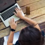 woman using laptop next to phone and coffee cup