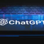 ChatGPT logo on a smart phone resting on a laptop keyboard, lit with a dark purple light