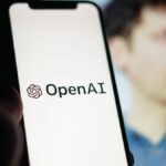 OpenAI logo on a phone screen in front of a blurred image of Sam Altman