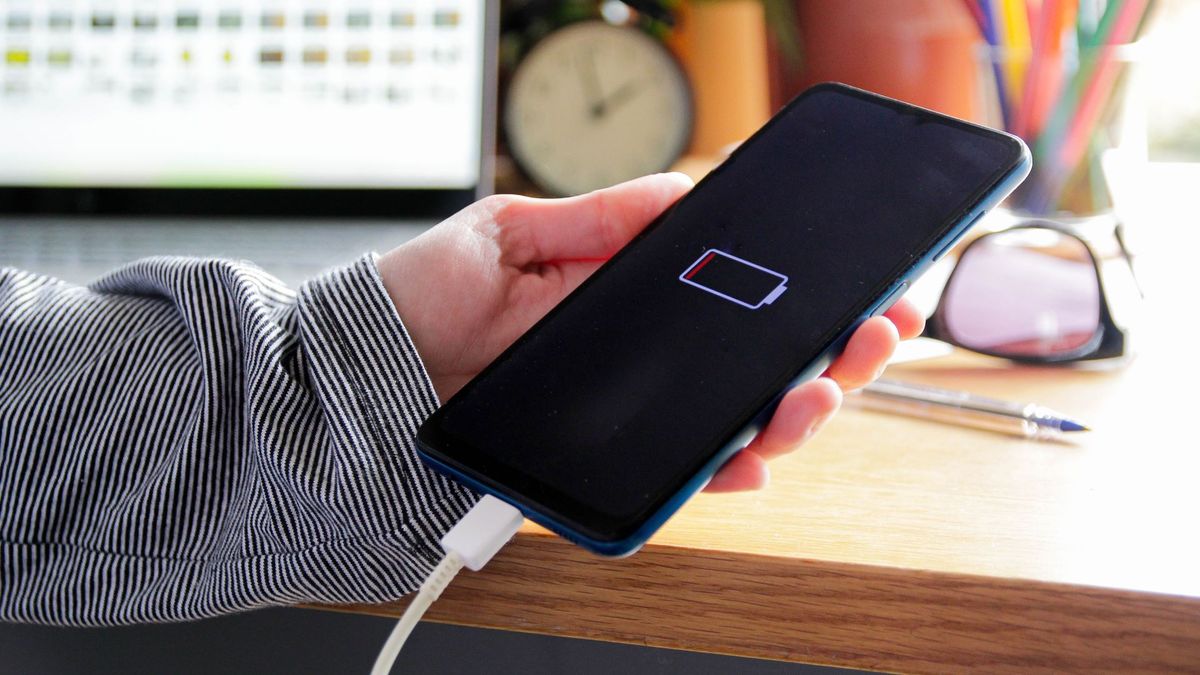 A person holding a phone which is displaying the no battery symbol