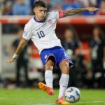 Christian Pulisic plays a pass ahead of the USA vs Canada live stream, wearing the USMNT white shirt and blues shorts.