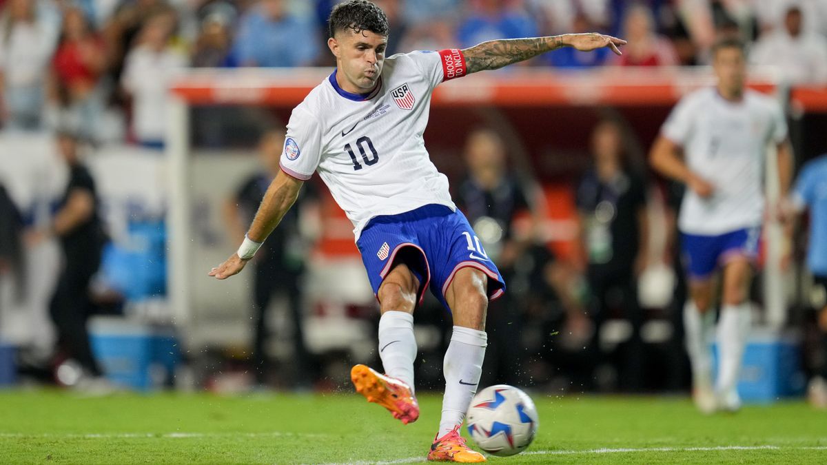 Christian Pulisic plays a pass ahead of the USA vs Canada live stream, wearing the USMNT white shirt and blues shorts.