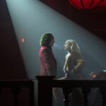 Arthur Fleck (Joaquin Phoenix) and Lee Quinzel (Lady Gaga) face one another lit by a spotlight in &quot;Joker: Folie A Deux&quot;