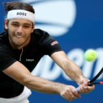 Taylor Fritz stretches for a backhand at the U.S. Open 2024 in a black t-shirt, white shorts and Hugo Boss headband.