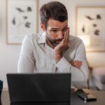 A man looking at his laptop in a stressed and upset manner