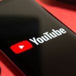 YouTube logo on smartphone flanked by earbuds