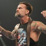 WWE wrestler CM Punk, wearing a black muscle vest, flexes his muscles to the crowd ahead of WWE Bad Blood 2024 live stream