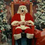 Art the Clown (David Howard Thornton) dressed as Santa Claus sitting on a throne flanked by Christmas trees and sacks of presents in &quot;Terrifier 3&quot;