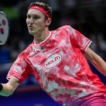 Viktor Axelsen of Denmark plays a shot in his red and white t-shirt and red headband.