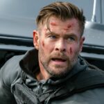 Chris Hemsworth, bruised, leans out of a helicopter in Extraction 2