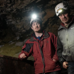 Ioan Lord and Al Tansey stand in a dark, rocky shaft wearing headlamps in Secrets of the Lost Mines