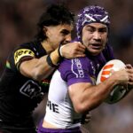 Jahrome Hughes (R), wearing white and purple kit and scrum cap, is tackled by Casey McLean (L), wearing black, in Panthers vs Storm NRL.