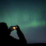 A photo of a person taking a photo of the Northern Lights on their phone