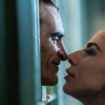 Arthur Fleck (Joaquin Phoenix) and Lee Quinzel (Lady Gaga) about to kiss through prison bars in &quot;Joker: Folie à Deux&quot;