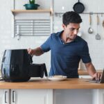 Man cooking with an air fryer while using a laptop