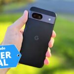 In-hand photo of the black Google Pixel 8a handset in front of outdoor setting with 'Killer Deal' badge overlaid.