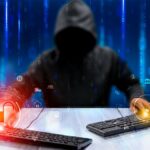 Hooded hacker sat at desk with two keyboards