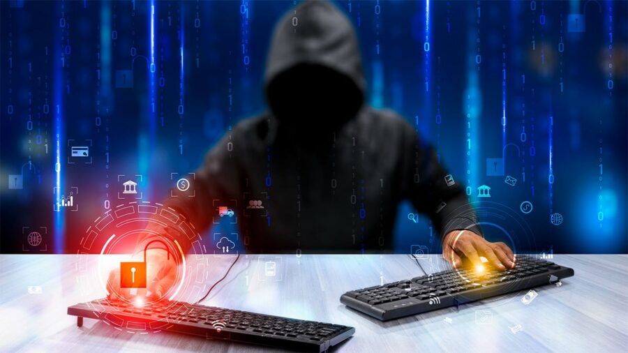 Hooded hacker sat at desk with two keyboards