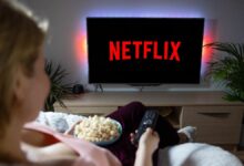 Woman with popcorn bowl holding remote to watch Netflix on television