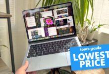 MacBook Air M4 in hand in room with plants in background with Tom's Guide Lowest Price badge